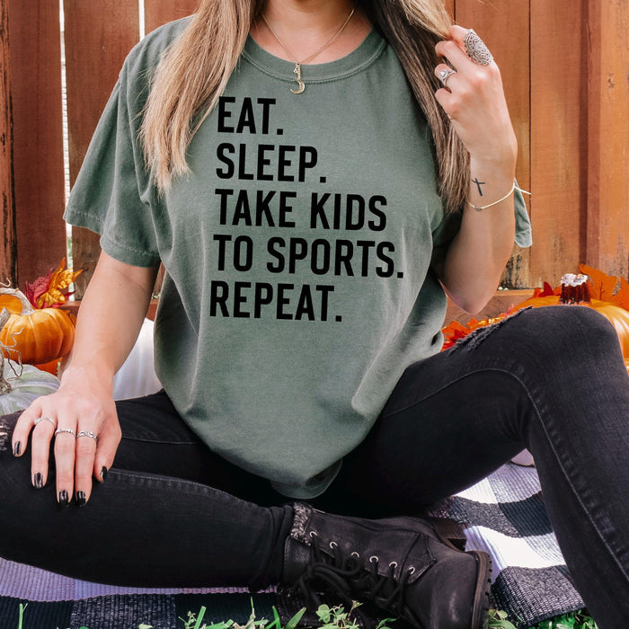 Dark green unisex graphic tee with black text: EAT SLEEP TAKE KIDS TO SPORTS REPEAT.